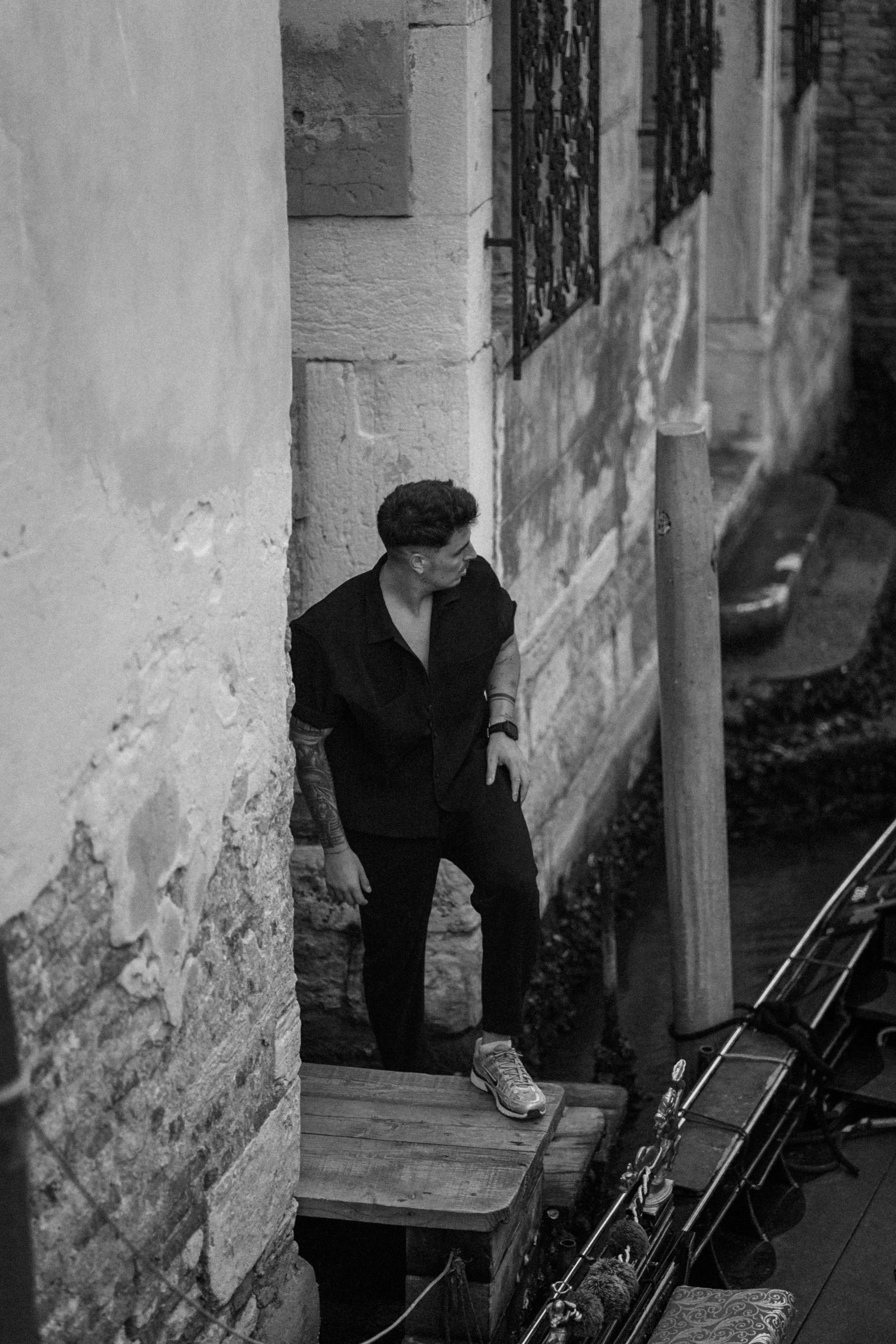 Retrato en blanco y negro de un hombre con ropa oscura junto a un muro de piedra